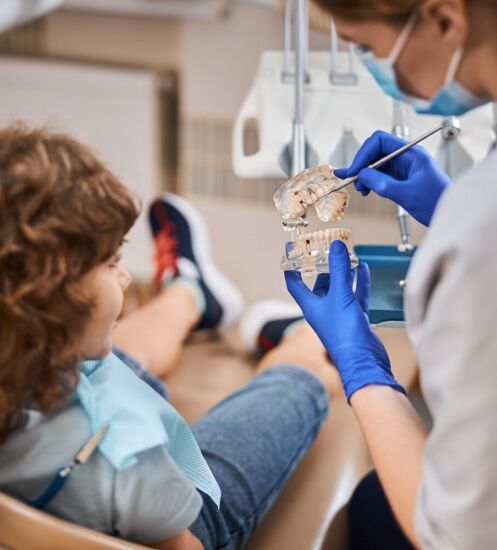 Pediatric dentist educating a child on dental hygiene while showing him a teeth prop in dentist office